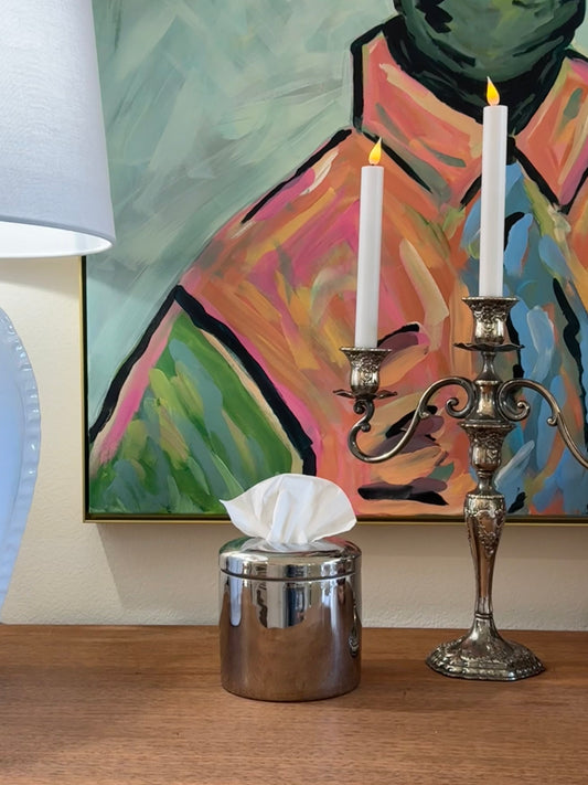 Sterling silver tissue vessel and candle holder on a table with a colorful abstract painting in the background.